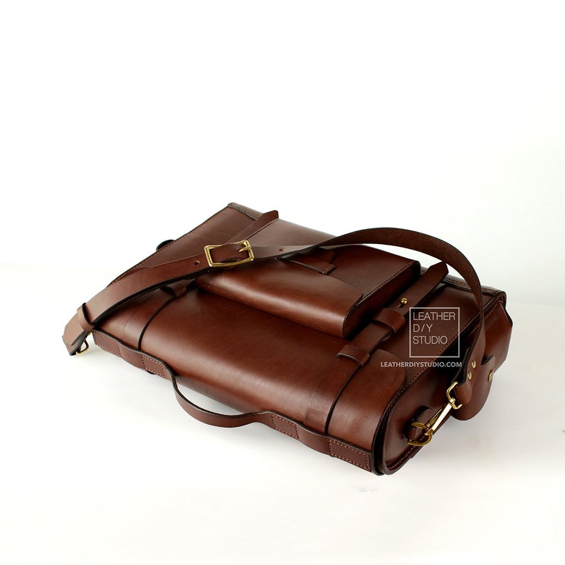 Puede incluir: Un bolso de cuero marr&oacute;n con una correa larga ajustable, un bolsillo frontal m&aacute;s peque&ntilde;o y una hebilla de lat&oacute;n. El bolso tiene una etiqueta que dice "Leather D/Y Studio" y "leatherdiystudio.com".