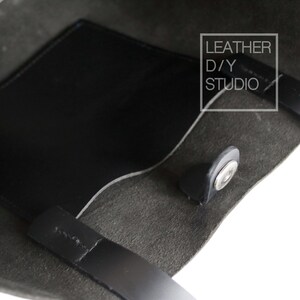 May include: A black leather tote bag with a black leather pocket on the inside. The bag has a snap closure and two black leather handles. The text "LEATHER D/Y STUDIO" is printed on a white rectangle on the bag.