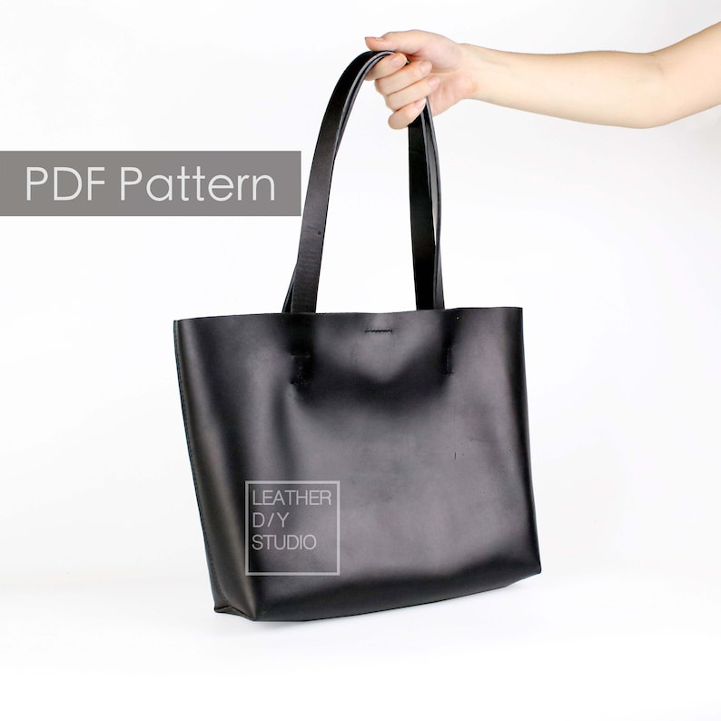 May include: A black leather tote bag with a simple design. The bag has two handles and a small label that reads "LEATHER D/Y STUDIO".