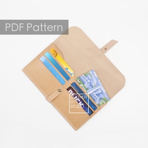 May include: A tan leather wallet with multiple card slots and a flap closure. The wallet is open and has several cards and a folded bill inside. The text "LEATHER D/CK STUDIO" is visible on the wallet.