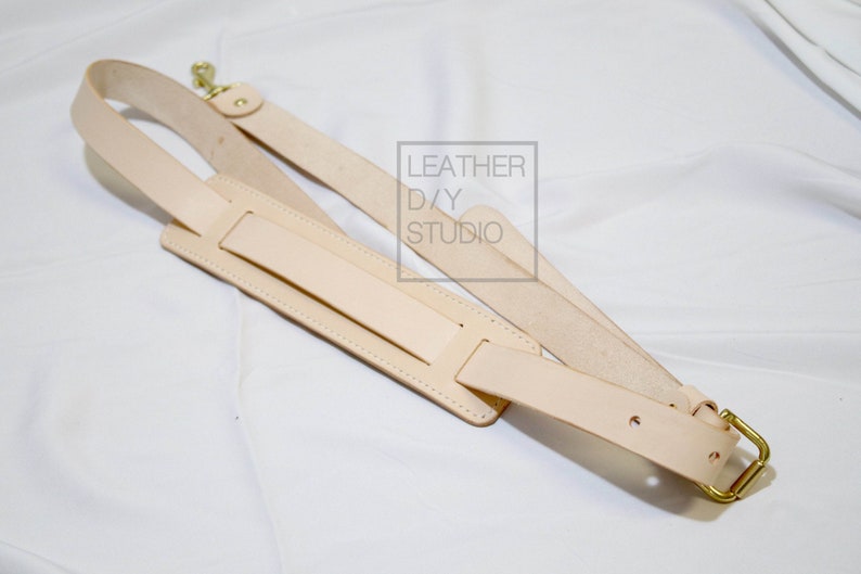 May include: A light brown leather camera strap with a gold metal buckle and two adjustable straps. The strap has the text "LEATHER D/Y STUDIO" printed on it.
