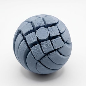 以下が含まれることがあります： 複雑なセグメントデザインの、3Dプリントされたライトブルーの球体。球体は、多数の立方体のようなセクションと湾曲したパネルで構成され、テクスチャード加工された表面を作り出しています。オブジェクトは無地の白い背景に配置されています。