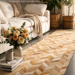 May include: A cowhide patchwork rug with a chevron pattern in shades of tan and cream. The rug is displayed in a living room setting with a white sofa, flowers, and plants. The text on the image reads "Natural Beauty. Timeless Comfort."