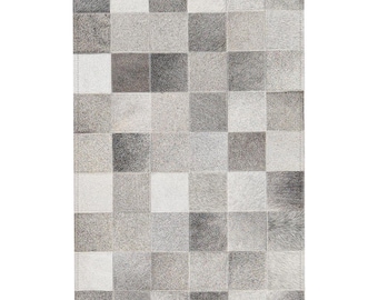 May include: A rectangular rug with a patchwork design. The rug is composed of numerous squares in varying shades of gray and white. The squares are arranged in a grid pattern, creating a textured surface. The rug is likely made of a natural material.