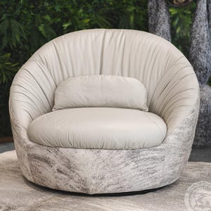 May include: A white leather swivel chair with a gray and white cowhide pattern on the base. The chair has a rounded back and a comfortable seat cushion.