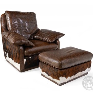 May include: A brown leather armchair with a matching ottoman. Both pieces are upholstered in a brown leather with a cowhide pattern. The chair has a high back and rolled arms. The ottoman is square and has a tufted top.