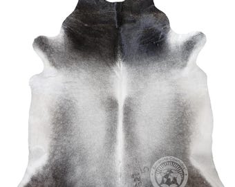 May include: A cowhide rug with a natural pattern of gray and white. The rug has a unique shape and texture, with a logo in the lower right corner. The rug is a decorative item for home decor.