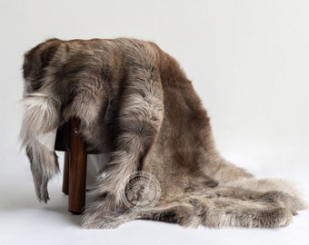 May include: A brown and gray sheepskin rug draped over a wooden stool. The rug has a soft, fluffy texture and is perfect for adding warmth and comfort to any room.