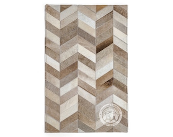 May include: A brown and white chevron patterned cowhide rug. The rug has a subtle distressed look and is made of natural leather. The rug is rectangular and has a fringe border. The rug is made by Sunshine Cowhides Worldwide.