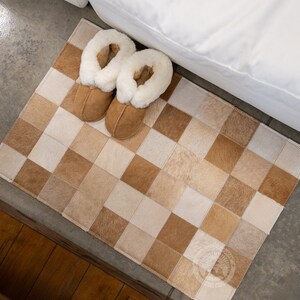 May include: A brown and white checkered rug made of cowhide with two brown slippers with white fur lining on top of it.