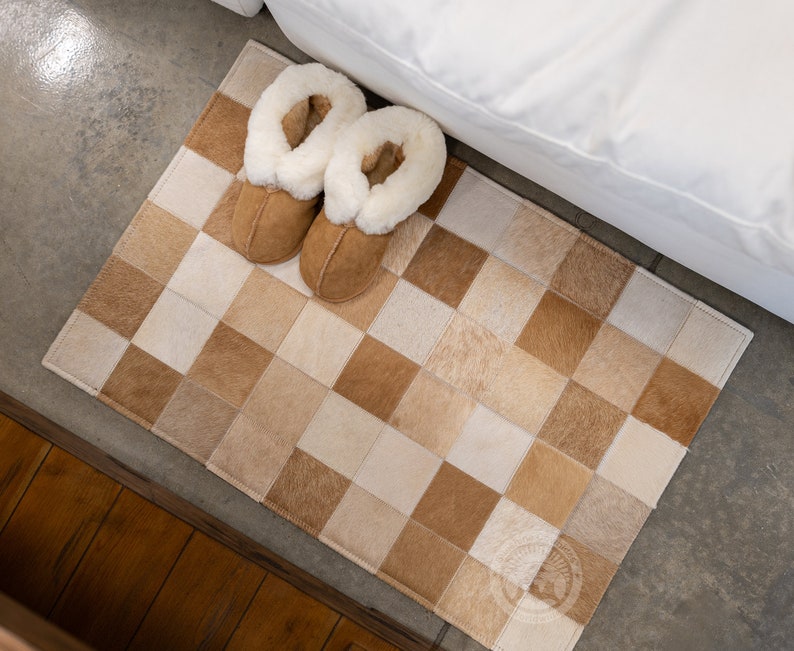 May include: A brown and white checkered rug made of cowhide with two brown slippers with white fur lining on top of it.