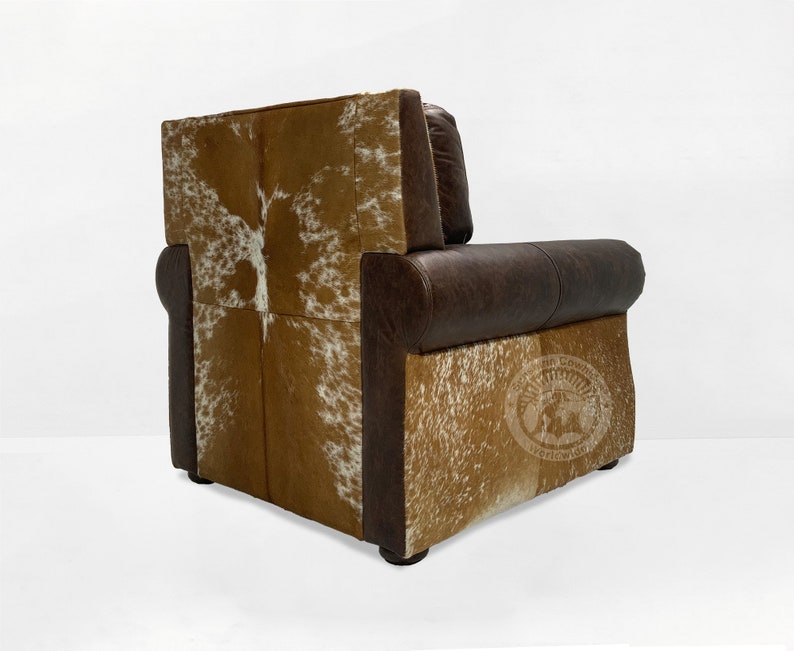 May include: A brown leather armchair with a cowhide back and seat. The chair has a tufted back and a rolled armrest. The chair is sitting on a white background.