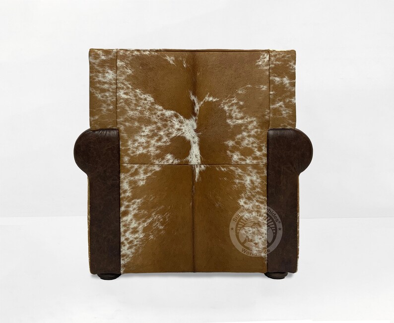 May include: A brown leather armchair with a white and brown cowhide pattern on the back and seat. The chair has a dark brown wooden frame and legs.