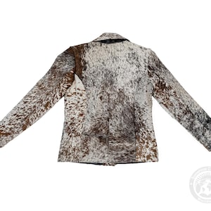 May include: A brown, white, and black cowhide blazer with a notched collar and long sleeves. The jacket has a classic tailored design and a natural, spotted pattern. The back view of the jacket is shown.