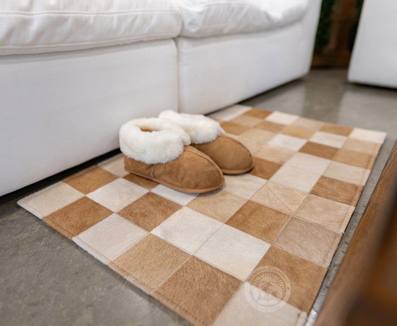 May include: A pair of brown suede slippers with white faux fur lining, placed on a brown and white checkered cowhide rug.