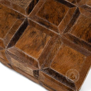 Pu&ograve; includere: Un pouf in pelle di mucca marrone e nero con un motivo geometrico. Il pouf &egrave; in pelle e ha una forma quadrata.