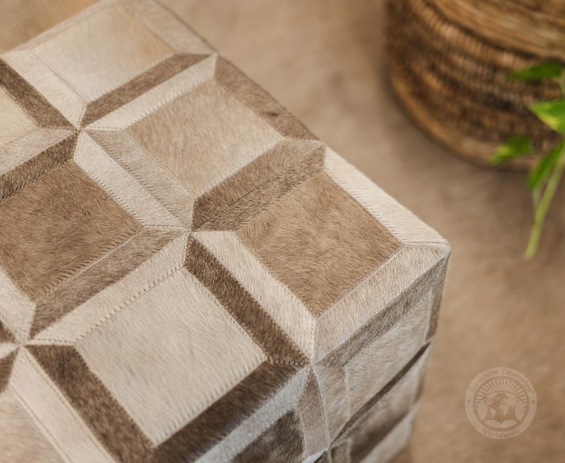 Pu&ograve; includere: Un pouf quadrato con un motivo geometrico in pelle di mucca marrone chiaro e bianco. Il pouf &egrave; realizzato con un patchwork di diversi pezzi di pelle, creando un design unico ed elegante.