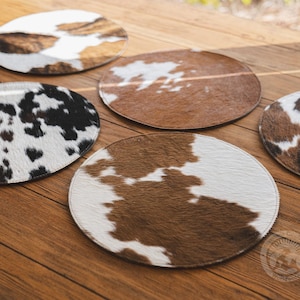 May include: A collection of circular coasters featuring various cowhide patterns in shades of brown, white, and black. Each coaster has a distinct animal print texture with stitched edges, displaying natural color variations across the set.