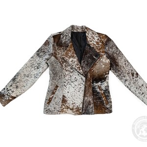May include: A cowhide jacket with a unique pattern of brown, white, and black patches. The jacket features a notched collar, a diagonal zipper closure, and two front pockets. The sleeves are long, and the jacket is fully lined.