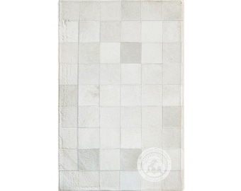 May include: Rectangular rug with a patchwork design. The rug is composed of numerous squares in varying shades of white and gray, creating a textured appearance. The edges are neatly stitched, and the overall aesthetic is modern and neutral.