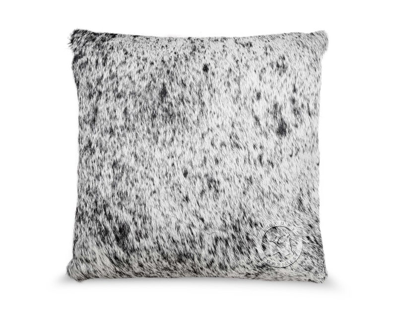 May include: A white and black cowhide pillow with a black leather tag that says "Cowhide" in white lettering.