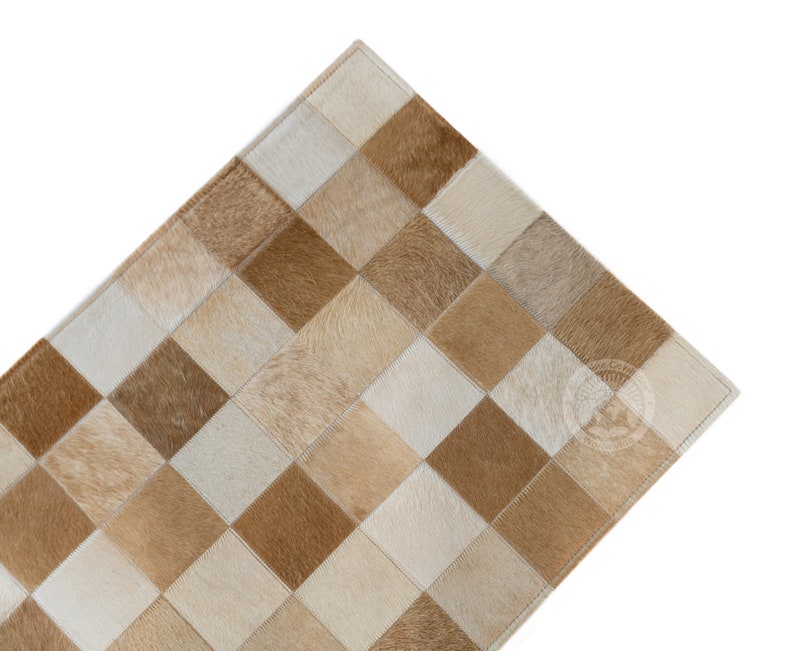 May include: A tan and white cowhide rug with a checkered pattern. The rug is made of individual squares of cowhide sewn together.