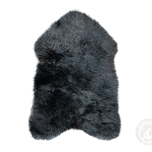 Puede incluir: Una alfombra de piel de oveja gris oscuro con un aspecto suave y texturizado. La alfombra tiene una forma irregular y probablemente est&aacute; hecha de piel de oveja natural. El color es un gris profundo y s&oacute;lido, adecuado para la decoraci&oacute;n del hogar.