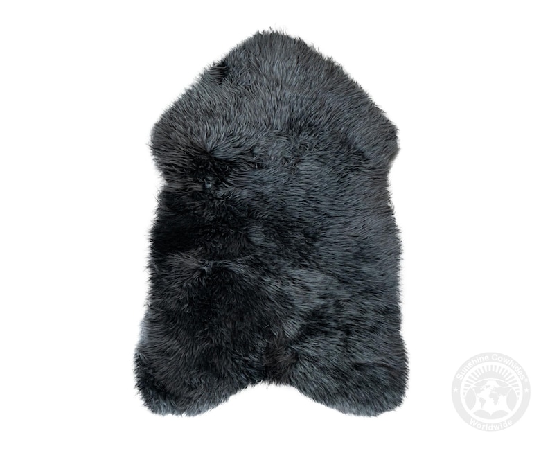 Puede incluir: Una alfombra de piel de oveja gris oscuro con un aspecto suave y texturizado. La alfombra tiene una forma irregular y probablemente est&aacute; hecha de piel de oveja natural. El color es un gris profundo y s&oacute;lido, adecuado para la decoraci&oacute;n del hogar.