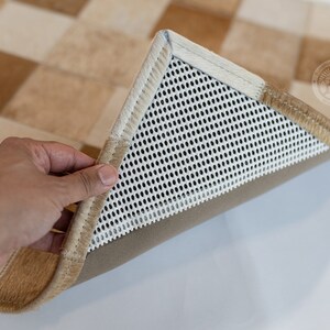 May include: Close-up of the underside of a tan and white checkered rug. The rug has a white mesh backing with a tan border.