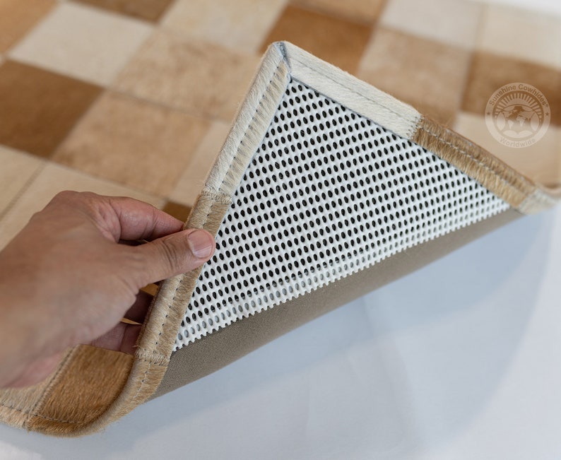 May include: Close-up of the underside of a tan and white checkered rug. The rug has a white mesh backing with a tan border.