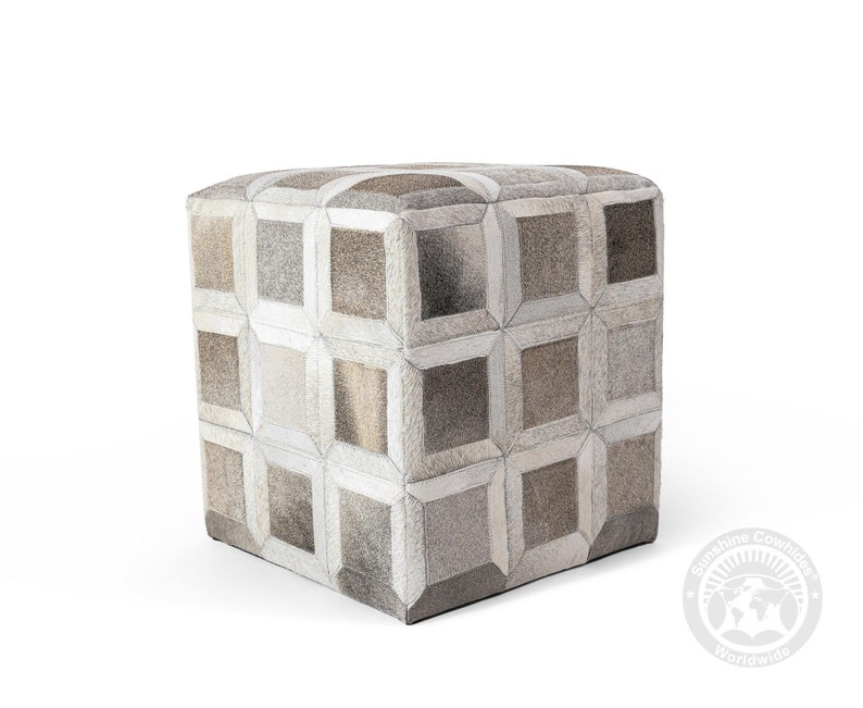 May include: A square ottoman with a geometric pattern made of cowhide in shades of gray and brown. The ottoman is sitting on a white surface.