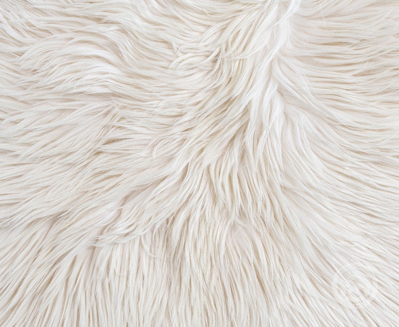 May include: A close-up view of long, soft, off-white faux fur material. The texture consists of dense, flowing synthetic fibers that create a shaggy, layered appearance with subtle variations in tone, ranging from cream to bright white throughout.