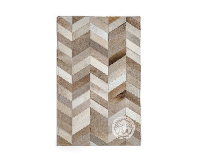 Pode incluir: Um tapete de pele de vaca com padr&atilde;o chevron marrom e branco. O tapete tem um visual desgastado sutil e &eacute; feito de couro natural. O tapete &eacute; retangular e tem uma borda de franjas. O tapete &eacute; feito por Sunshine Cowhides Worldwide.