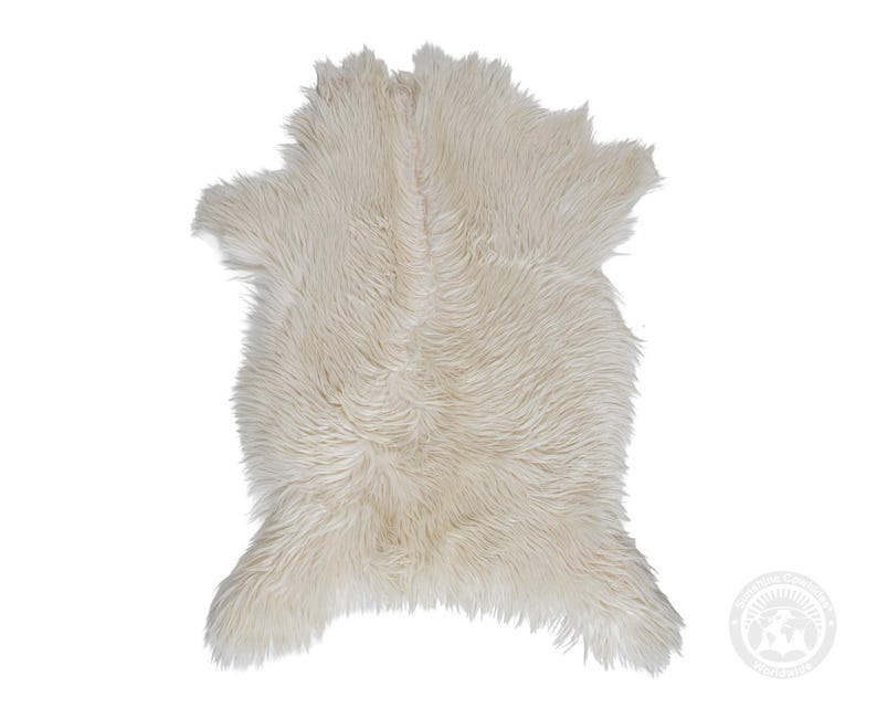 May include: A cream-colored faux fur rug with a long, shaggy pile texture. The rug features an irregular, organic shape with a central seam running vertically down the middle, creating a soft, layered appearance across the entire surface.