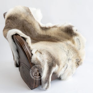 May include: A reindeer hide draped over a brown leather chair. The hide features a mix of light brown, grey, and white fur. The chair's leather is a dark, rich brown. The hide is soft and fluffy, adding texture to the scene.