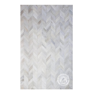 Puede incluir: Alfombra de piel de vaca blanca con un patrón de chevron. La alfombra está hecha de cuero natural y tiene una sensación suave y lujosa.