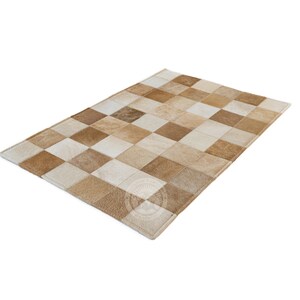 May include: A patchwork rug made of different shades of brown and white leather. The rug is made up of squares of leather sewn together.