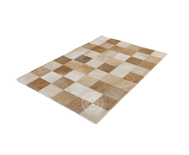 May include: A patchwork rug made of different shades of brown and white leather. The rug is made up of squares of leather sewn together.