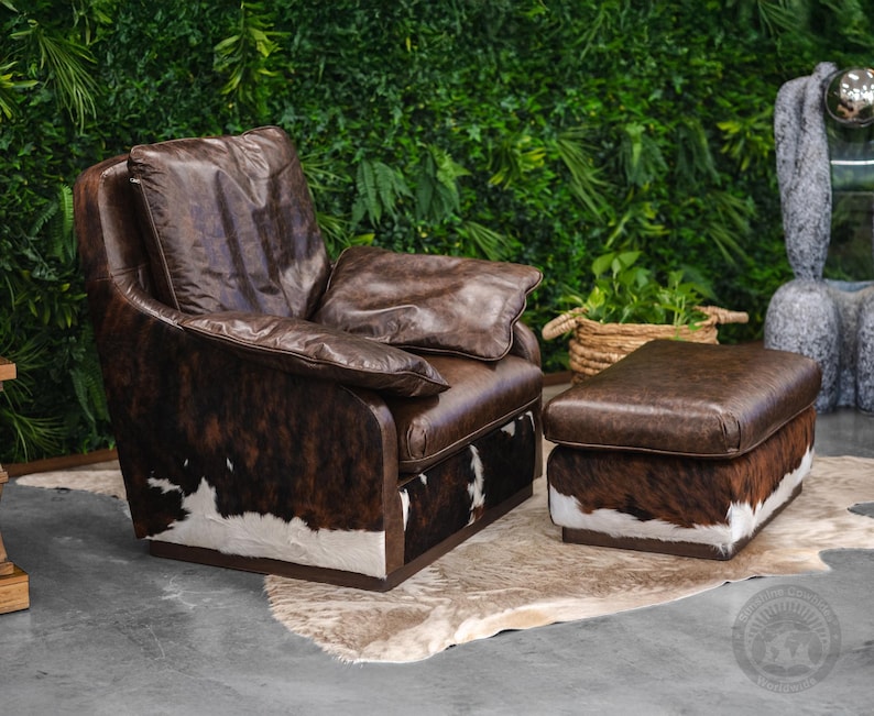 May include: A brown leather armchair with a white and brown cowhide pattern. The armchair has a matching ottoman with a brown leather top and a white and brown cowhide base. The armchair and ottoman are sitting on a white rug.