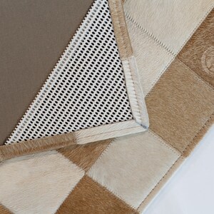 May include: A close-up of a brown and white checkered rug with a brown leather border. The rug has a white mesh backing.