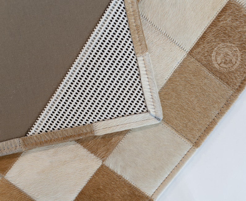 May include: A close-up of a brown and white checkered rug with a brown leather border. The rug has a white mesh backing.