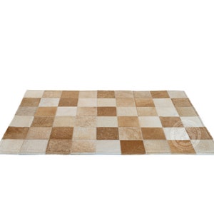 May include: A tan and white patchwork rug made of cowhide. The rug is made up of squares of different sizes and colors.