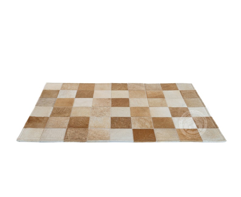 May include: A tan and white patchwork rug made of cowhide. The rug is made up of squares of different sizes and colors.