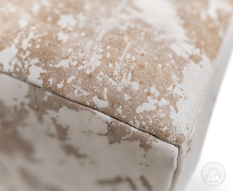 Puede incluir: Un objeto rectangular que presenta una superficie texturizada con un patr&oacute;n moteado de colores beige claro y blanco roto. El material muestra una apariencia desgastada y envejecida con parches de color irregulares distribuidos por la parte superior plana y el lateral.