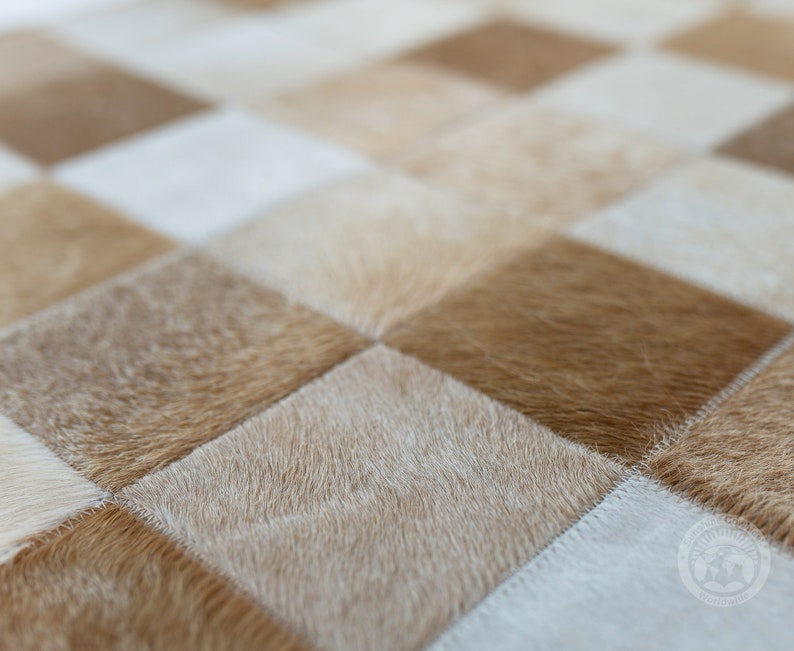 May include: A close-up of a checkered cowhide rug with alternating light and dark brown squares. The rug is made of soft, natural cowhide and has a unique, rustic look.