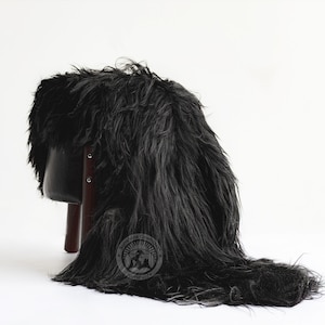Puede incluir: Un accesorio de piel sint&eacute;tica negra, drapeado sobre un taburete peque&ntilde;o. La piel es larga y peluda, creando un efecto dram&aacute;tico. El taburete tiene un asiento negro y patas de color marr&oacute;n oscuro. El accesorio se utiliza probablemente para fotograf&iacute;a o decoraci&oacute;n.