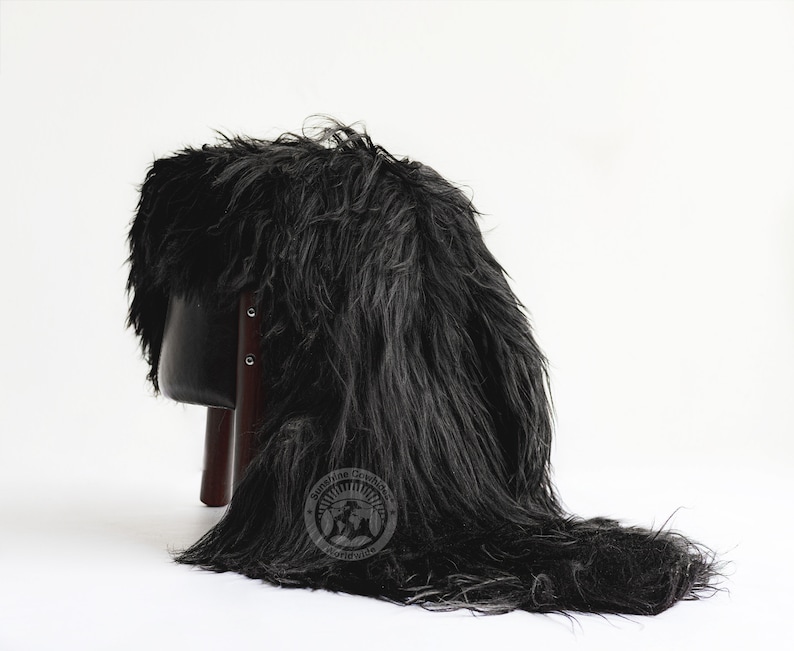 Puede incluir: Un accesorio de piel sint&eacute;tica negra, drapeado sobre un taburete peque&ntilde;o. La piel es larga y peluda, creando un efecto dram&aacute;tico. El taburete tiene un asiento negro y patas de color marr&oacute;n oscuro. El accesorio se utiliza probablemente para fotograf&iacute;a o decoraci&oacute;n.