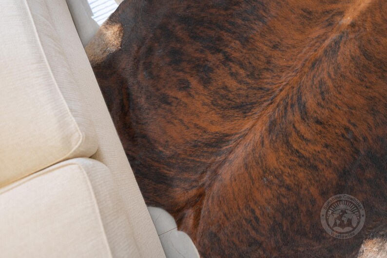 May include: Close-up of a brown and black cowhide rug with a white couch in the background.