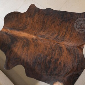 May include: A brown and black cowhide rug with a natural, mottled pattern. The rug is made of real cowhide and has a soft, luxurious feel.