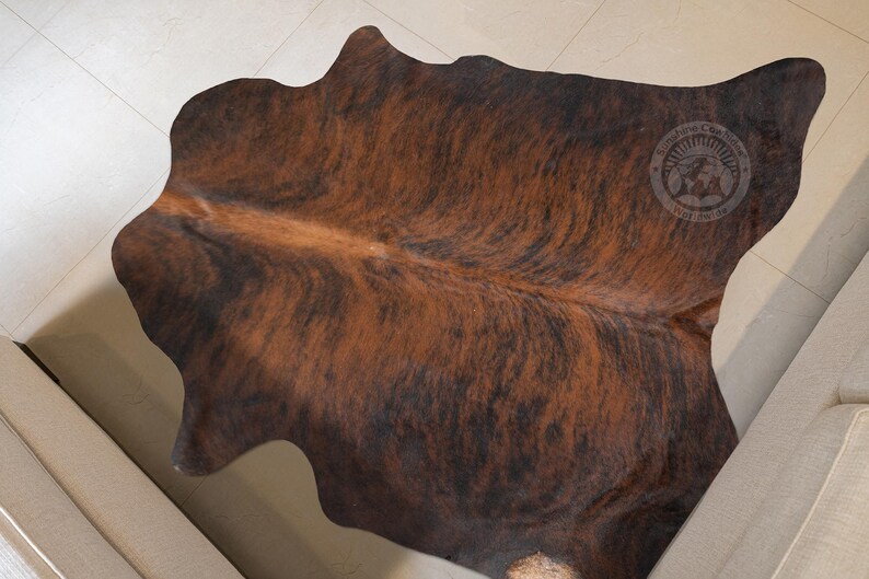 May include: A brown and black cowhide rug with a natural, mottled pattern. The rug is made of real cowhide and has a soft, luxurious feel.